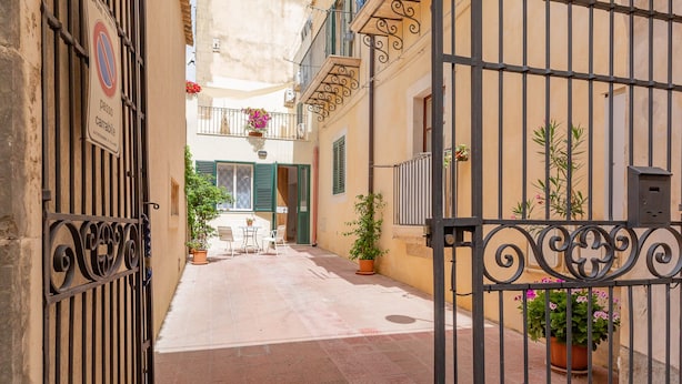 A narrow alleyway with a gated entrance, potted plants, and a table with chairs. - House in the historic center with private terrace and patio (Noto)