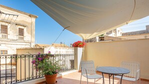 A balcony with a table and chairs, a potted plant, and a view of neighboring buildings. - House in the historic center with private terrace and patio (Noto)