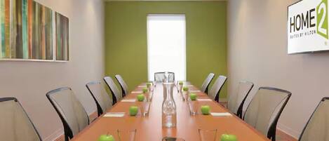 A conference room with a long table, chairs, and green apples.