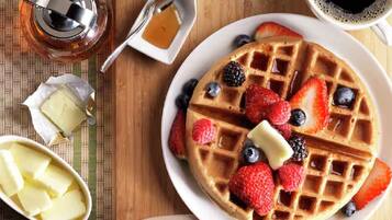 A breakfast setting with waffles topped with berries and syrup, a small bowl of butter, and a cup of coffee.