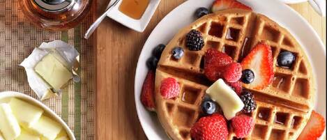 A breakfast setting with waffles topped with berries and syrup, a small bowl of butter, and a cup of coffee.