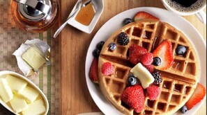 A breakfast setting with waffles topped with berries and syrup, a small bowl of butter, and a cup of coffee. - Home2 Suites By Hilton Racine (Sturtevant)