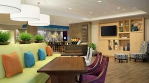 A modern hotel lobby with a seating area, a bar, and a television. - Home2 Suites By Hilton Racine (Sturtevant)