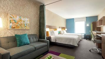 A hotel room with a sofa, two beds, a desk, and a painting on the wall.