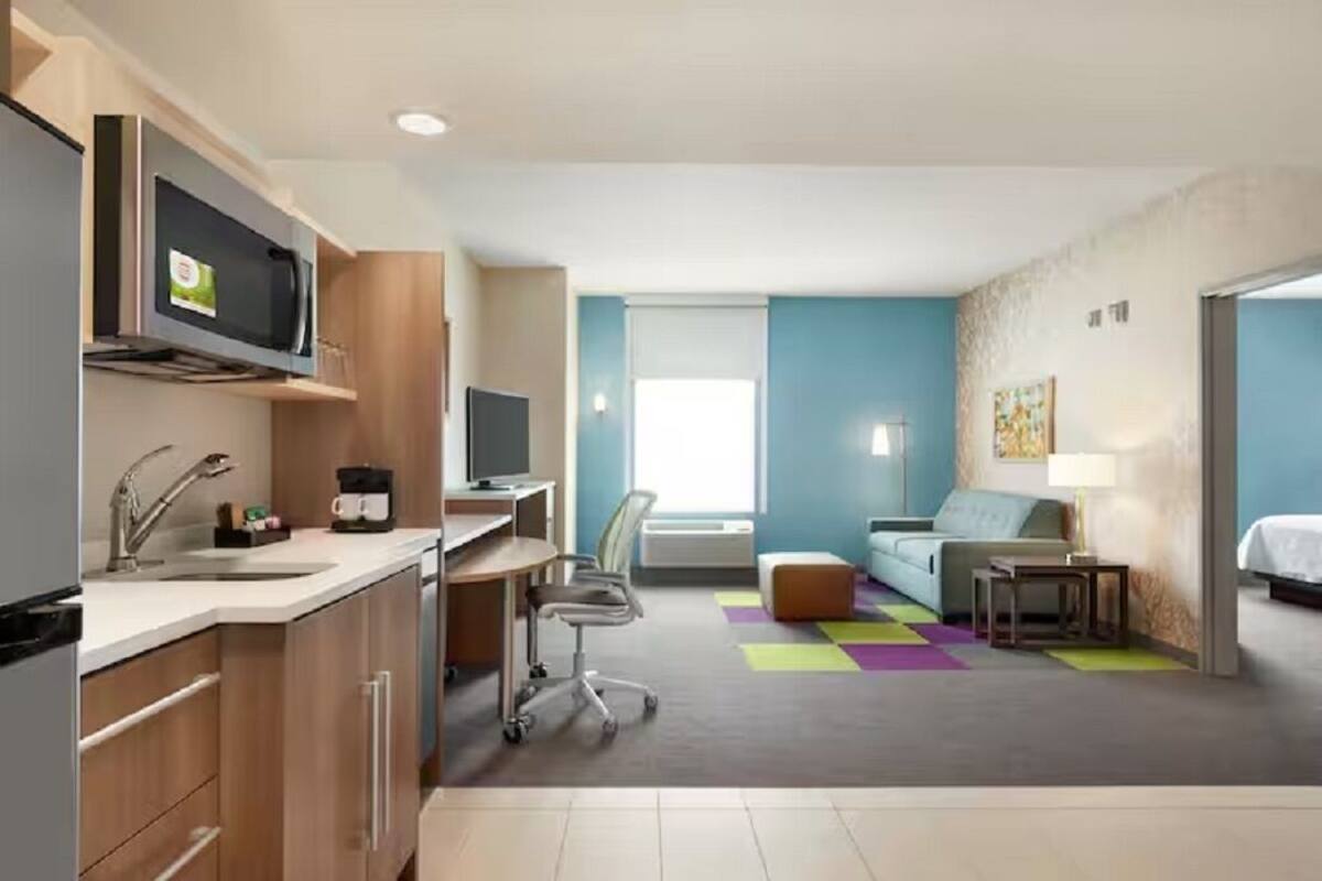 A compact hotel room with a kitchenette, a sofa, a desk, and a television.