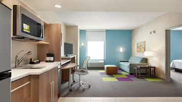 A compact hotel room with a kitchenette, a sofa, a desk, and a television.