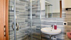 Une salle de bain moderne avec une douche à parois de verre, un lavabo surmonté d’un miroir et un mur décoré d’un motif imitant le marbre.