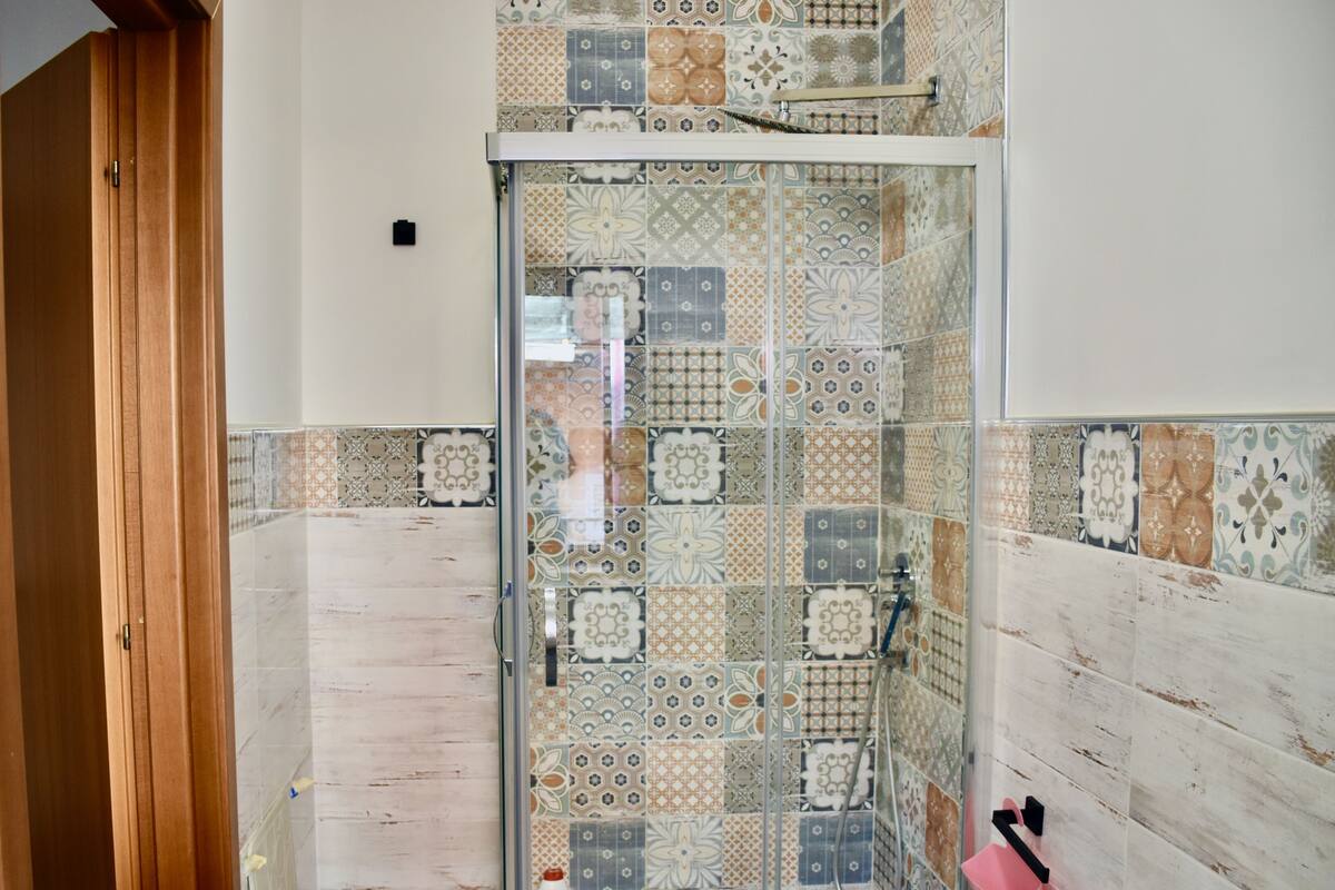 Un baño con zona de ducha, paredes de azulejos y una puerta de madera.