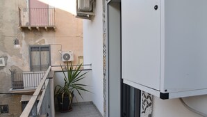 Un étroit couloir extérieur agrémenté d’un pot de fleurs, d’une rambarde en métal et d’une porte donnant sur une pièce.