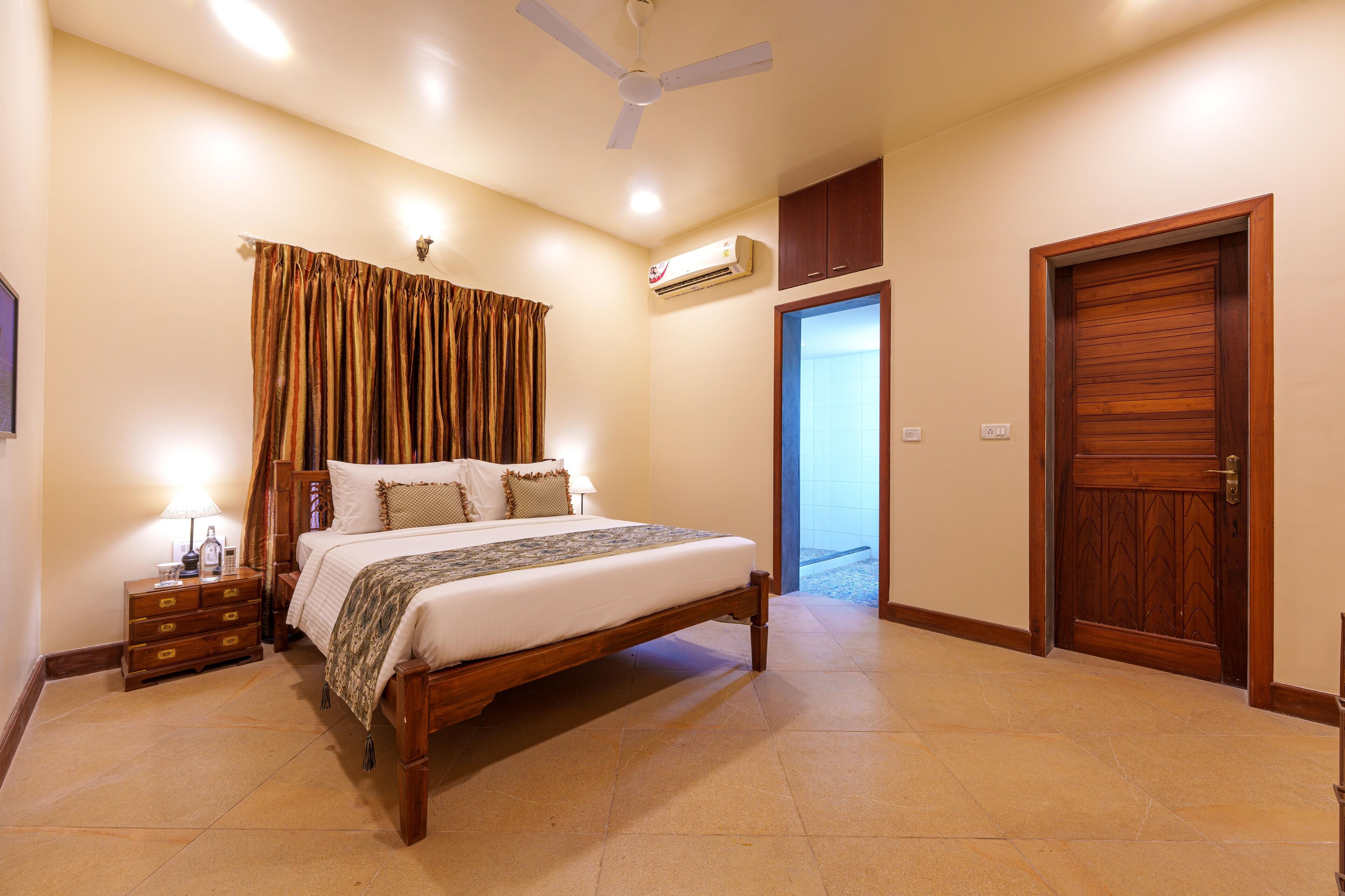 A bedroom with a bed, a nightstand, a dresser, an air conditioning unit, a ceiling fan, and a wooden door.