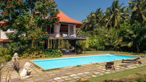 A poolside area with a clear blue pool, a covered patio, and a statue of a lion. - Amã Stays & Trails Skyfall, Kashid (Murud)