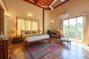 A bedroom with a bed, bedside tables, a desk, and a chair. There is a window with curtains and an air conditioning unit on the wall. - Amã Stays & Trails Skyfall, Kashid (Murud)