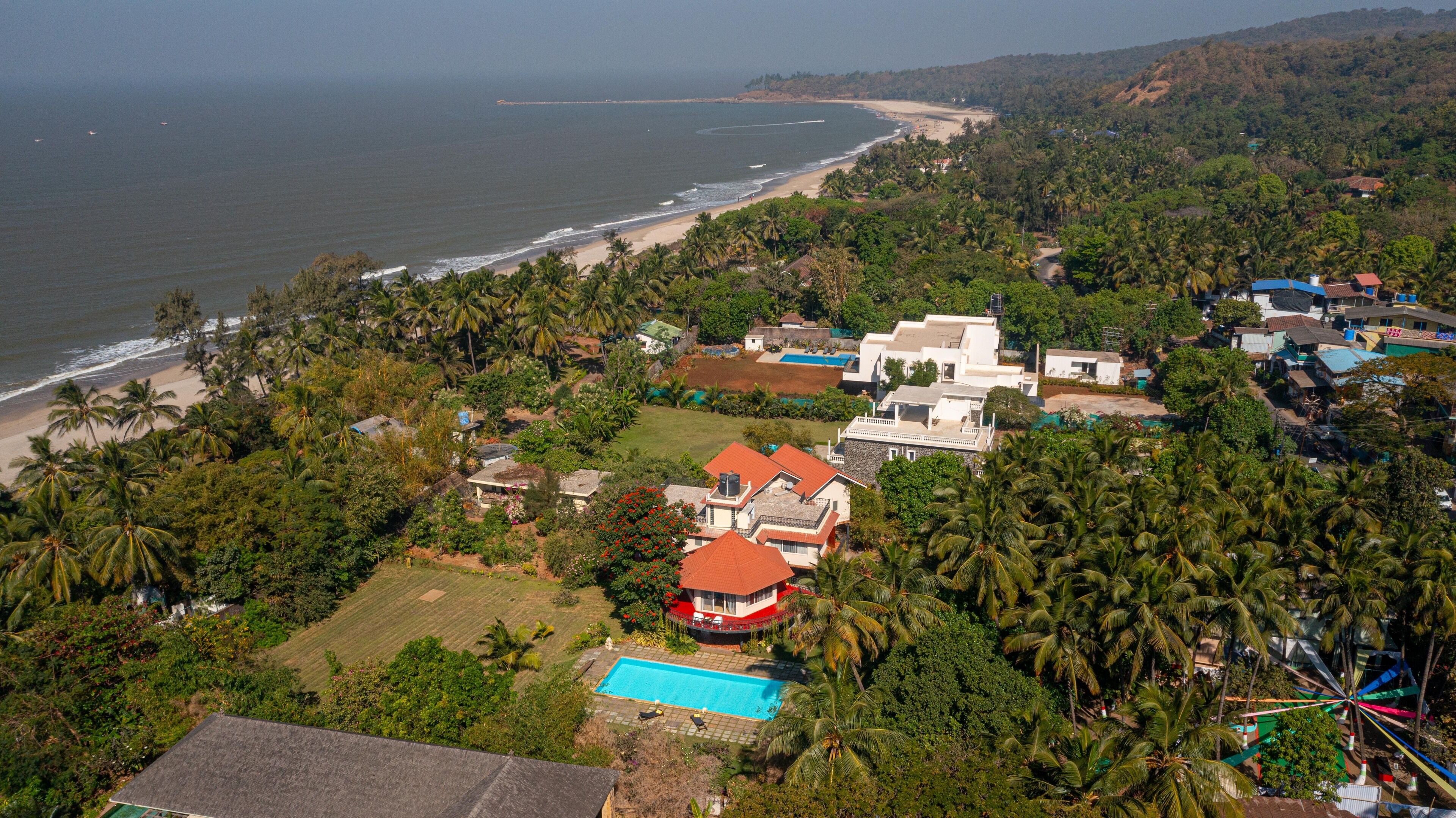 An aerial view of a coastal area with a beach, houses, and a swimming pool.