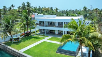 Uma casa moderna de dois andares com piscina, cercada por vegetação exuberante e palmeiras.