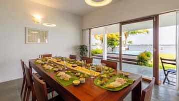 Mesa de jantar posta com comida e bebidas, janelas amplas e vista para o exterior.