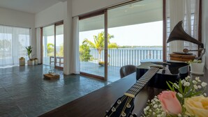 A spacious room with a large window overlooking a balcony with a view of palm trees and the sea. - Amã Stays & Trails Anchorage Vypin, Cochin (Kochi)