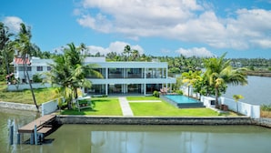 A modern two-story house with a swimming pool, surrounded by palm trees and a body of water. - Amã Stays & Trails Anchorage Vypin, Cochin (Kochi)