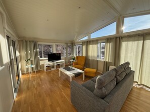 A spacious living room with a large window, wooden flooring, a grey sofa, a yellow armchair, and a television on a white stand. - Family-friendly Swedish house in a quiet and central location (Västra Götalands län)
