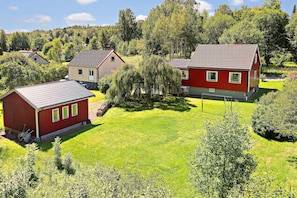 A residential area with two main houses, one red and one beige, surrounded by lush greenery and trees. - Family-friendly Swedish house in a quiet and central location (Västra Götalands län)