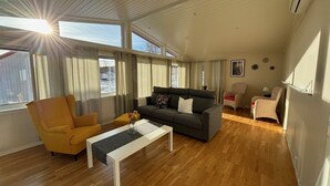 Een ruime woonkamer met een houten vloer, een grijze bank, een gele fauteuil en een witte salontafel.
