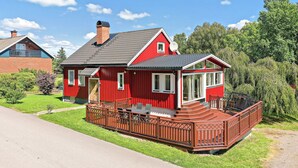 Een rode, twee verdiepingen tellende woning met een balkon en een terras.