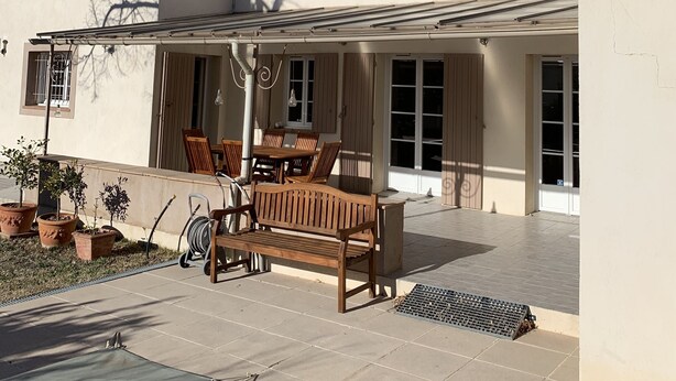 Un bâtiment à deux étages doté d’un patio couvert, d’une table à manger et de plusieurs plantes en pot.