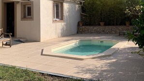 Une petite maison avec une piscine, un mur en pierre et des plantes en pot.