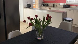 Une cuisine moderne équipée d’un réfrigérateur Samsung, d’une table à manger ornée d’un vase de tulipes rouges et d’une fenêtre avec des stores.
