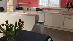 Une cuisine moderne avec des meubles blancs, un mur d’accent rouge et une fenêtre équipée de stores.