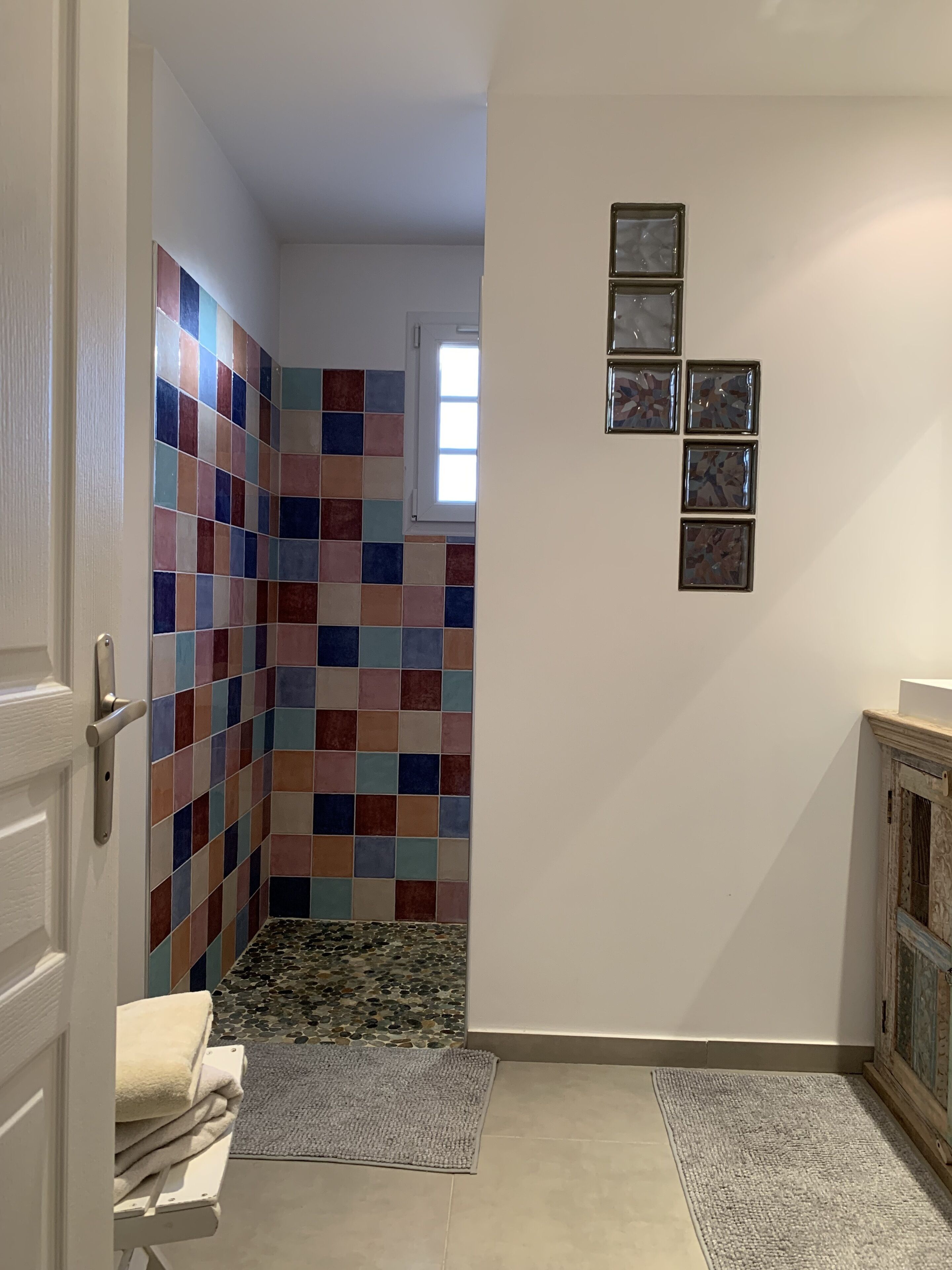 Une salle de bain avec des carreaux de mosaïque aux couleurs vives, une petite fenêtre et une porte dotée d’un porte-serviettes.