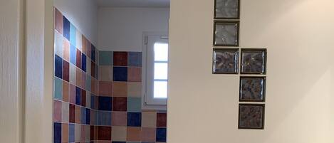 Une salle de bain avec des carreaux de mosaïque aux couleurs vives, une petite fenêtre et une porte dotée d’un porte-serviettes.
