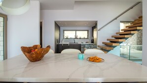 A modern kitchen with a marble island, wooden chairs, and a staircase with wooden steps. - SeaWhisper Villa - Four Bedroom Villa, Sleeps 8 (Paxi)