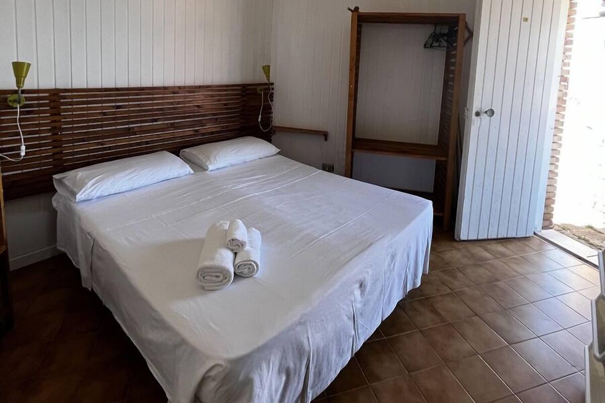 A bedroom with a large bed, white linens, a wooden headboard, a ceiling fan, and a door leading to a balcony.