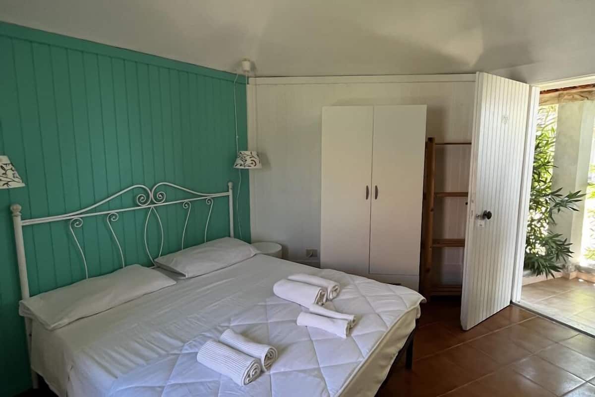 A bedroom with a bed, a ceiling fan, a wardrobe, and a door leading to an outdoor area.