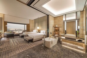 A hotel room with a large bed, a sitting area, a bathtub, and a city view.