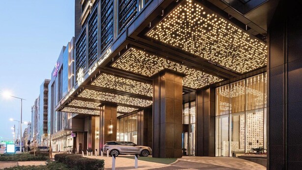A modern hotel entrance with a covered walkway, large windows, and a car parked outside.