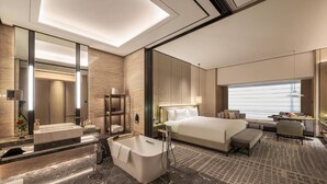 A modern hotel room with a large bed, a separate sitting area, a bathtub, and a large window providing a view.