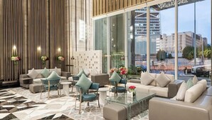 A modern lobby with a geometric patterned floor, a seating area with sofas and chairs, and large windows offering a view of the cityscape.