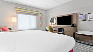 Ein Hotelzimmer mit einem großen Bett, einem Schreibtisch mit Computer, einem Flachbildfernseher und einem Fenster mit Jalousien.