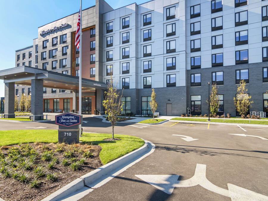 Edifício do Hampton Inn & Suites by Hilton com design moderno, gramado bem cuidado e sinalização direcional clara.