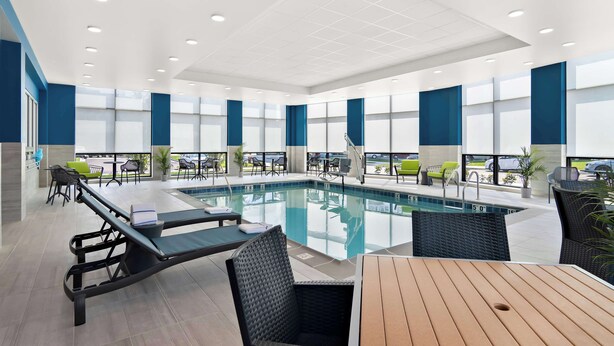 A modern indoor pool area with lounge chairs, a wooden table, and large windows. - Hampton Inn & Suites Chicago Medical District UIC (Chicago)