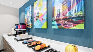 A hotel reception area with a counter displaying pastries and coffee, a coffee machine, and a golden clock. - Hampton Inn & Suites Chicago Medical District UIC (Chicago)