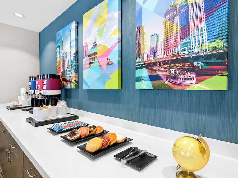 Ein Hotel-Rezeptionsbereich mit einer Theke, auf der Gebäck und Kaffee angeboten werden, einer Kaffeemaschine und einer goldenen Uhr.