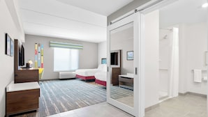 A modern hotel room with a large bed, a desk, a chair, a TV, and a sliding door leading to a shower area. - Hampton Inn & Suites Chicago Medical District UIC (Chicago)