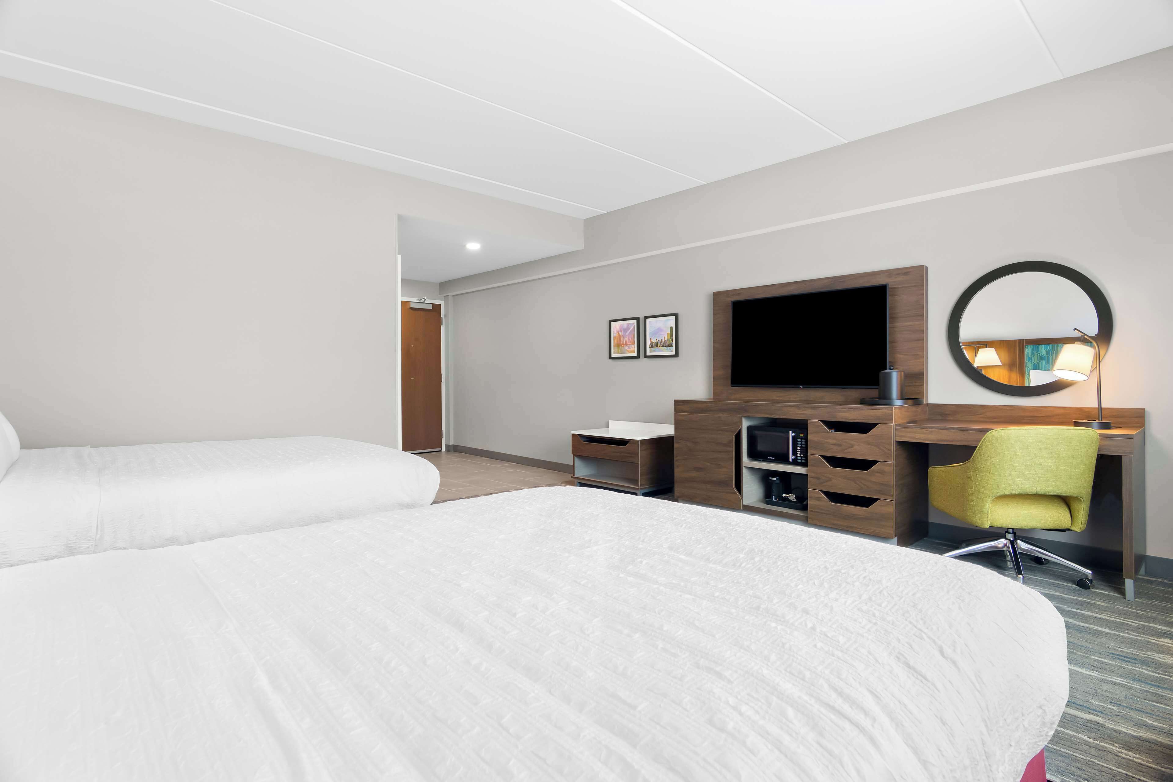 Una habitación de hotel con dos camas, un escritorio, un televisor de pantalla plana, un espejo y una silla.