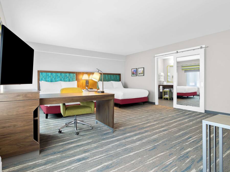 Hotelkamer met een bureau, twee bedden, een televisie en een badkamer met spiegel en toilet.