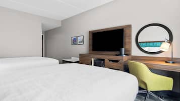 Habitación de hotel con dos camas, un escritorio con silla, televisor, espejo y lámpara.