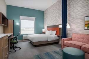 A hotel room with a bed, a desk, a chair, a sofa, and a window.