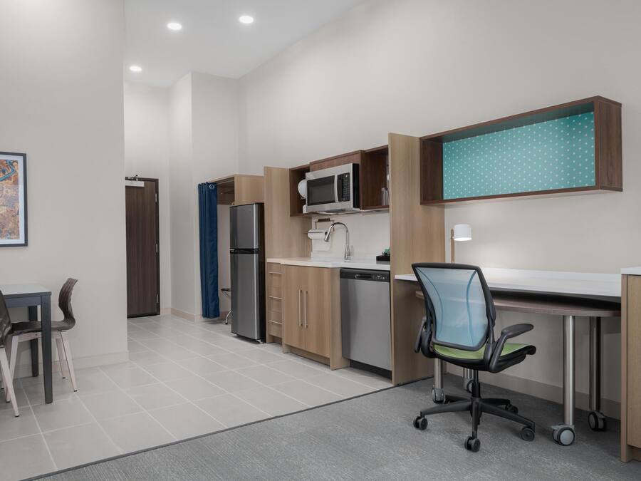 A modern kitchen with built-in appliances, a dining area with a table and chairs, and a workspace with a desk and chair.