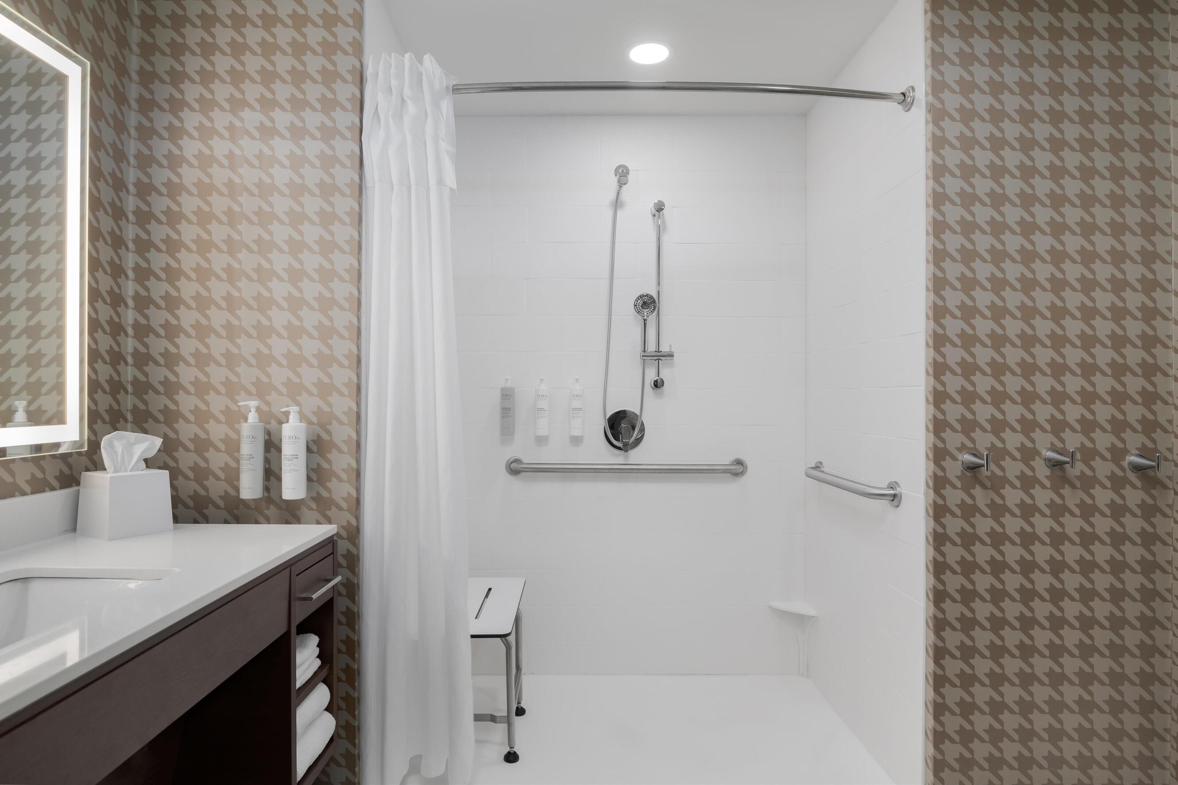 Une salle de bain moderne équipée d’une douche, d’un meuble-lavabo avec miroir et de produits de toilette.